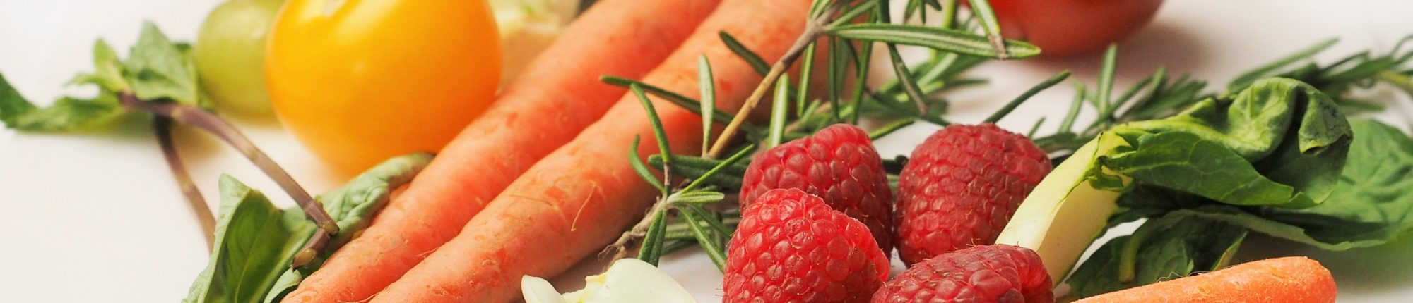 A pile of carrots, raspberries, chard, walnuts, and tomatoes on a white background