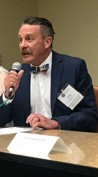 Dr. Garrow sits at a table speaking into a microphone that he is holding