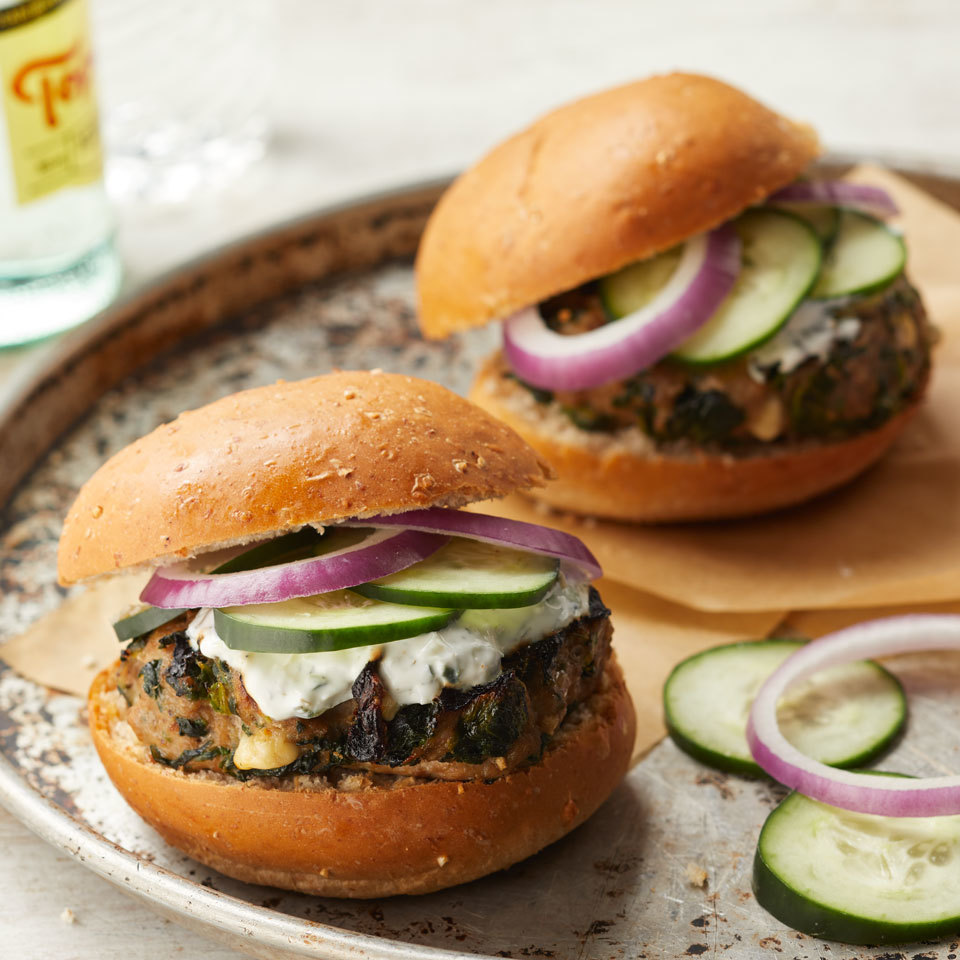 Close-up of two turkey burgers with red onion, tzatziki sauce, and cucumbers on whole wheat buns