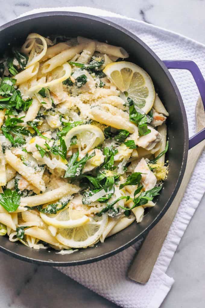 Cast iron skillet filled with chicken spinach pasta with lemon slices and parmesan cheese