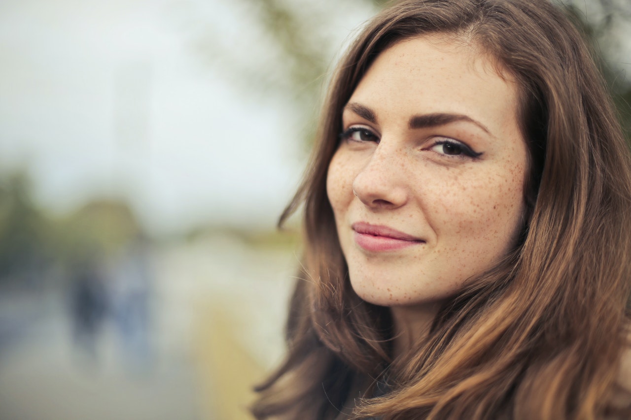 Close up of a woman's face. She has brown hair, dark eyes, and freckles. The background is distorted