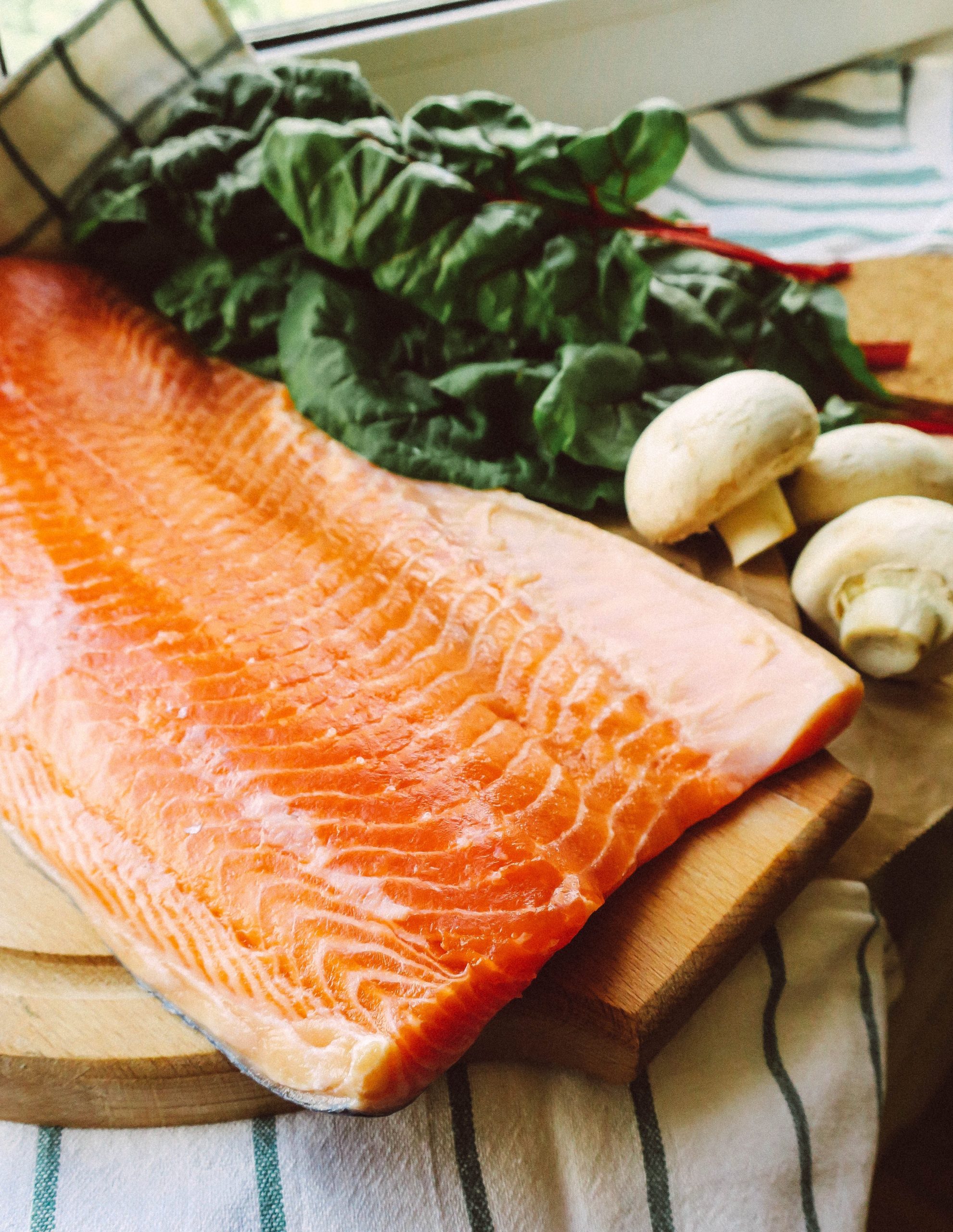 A close-up of cooked fish on a cutting board next to a pile of Swiss chard and mushrooms