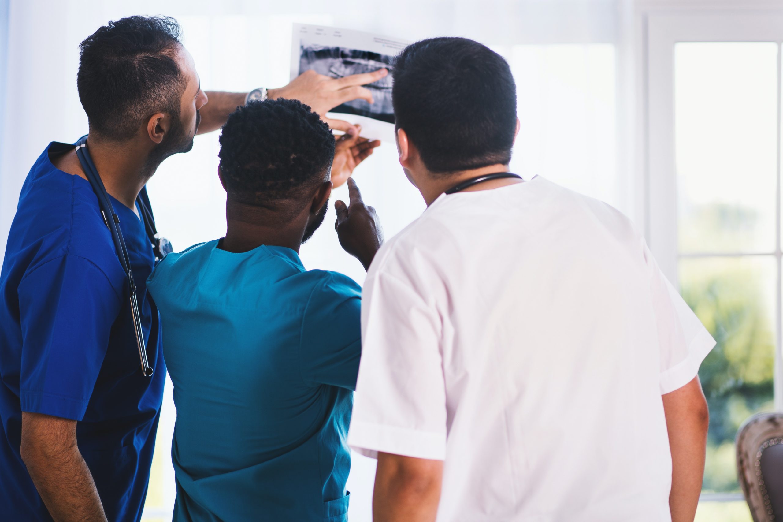 Three male nurses examine an ultrasound image, pointing at and discussing it