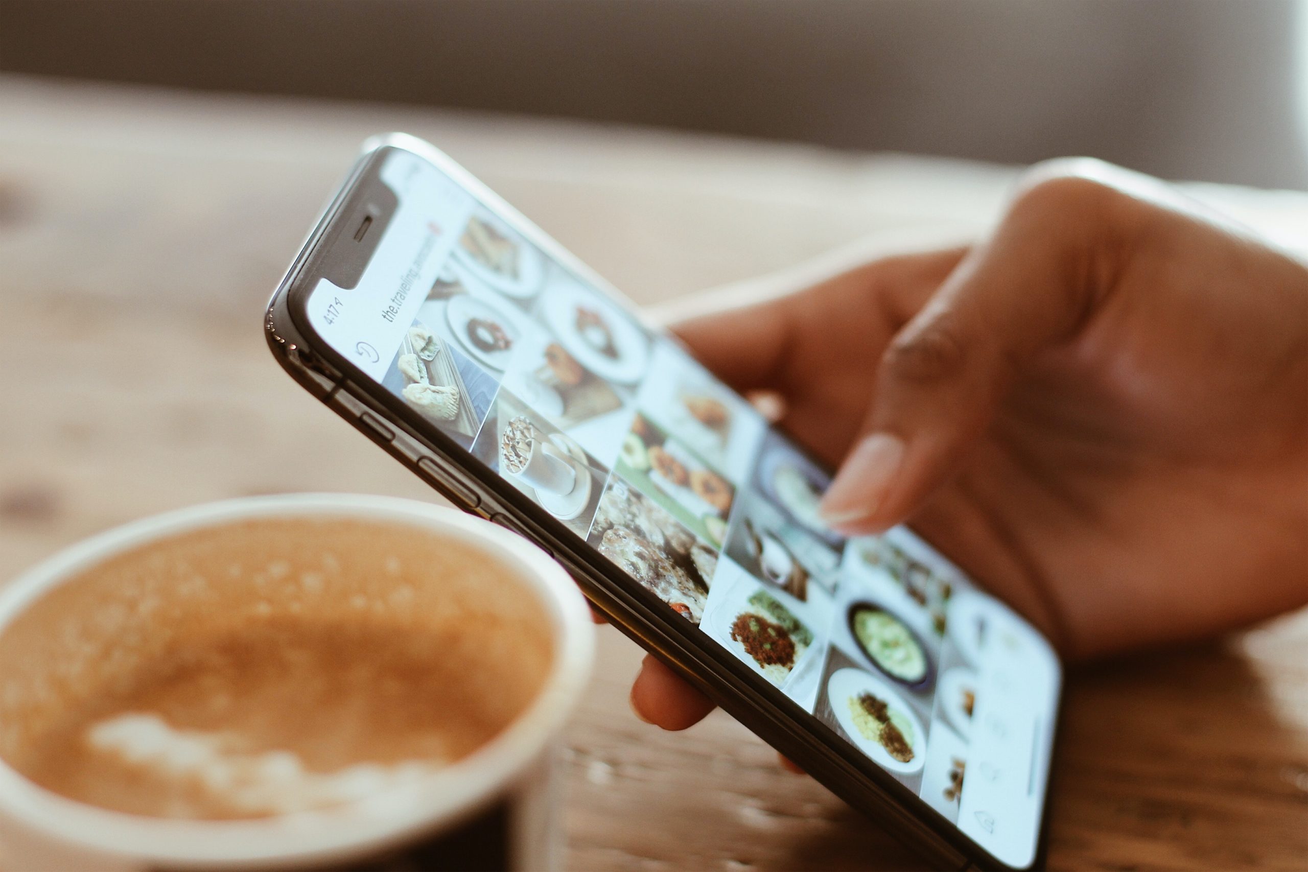 A close-up of a person scrolling through Instagram on their phone next to a cup of coffee