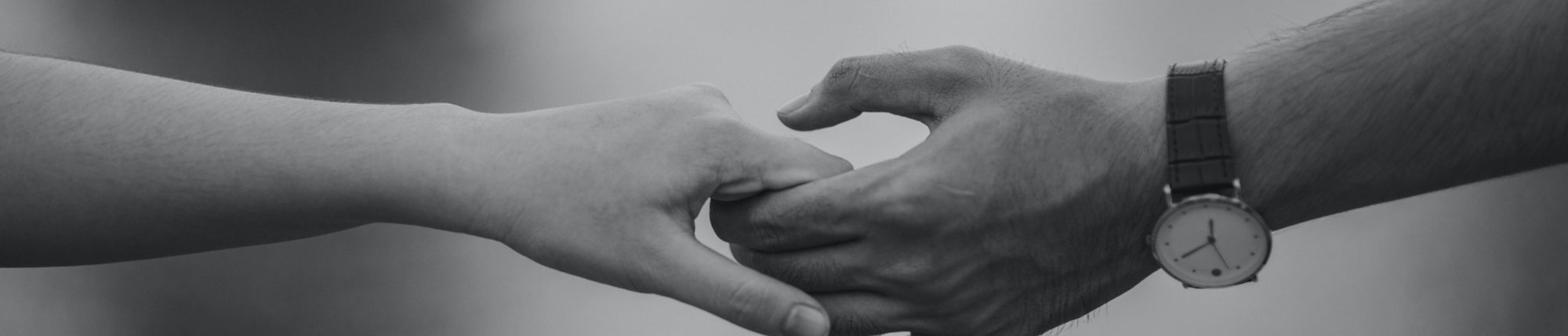 Black and white photo of a woman and man holding hands. The man has a watch on his arm.