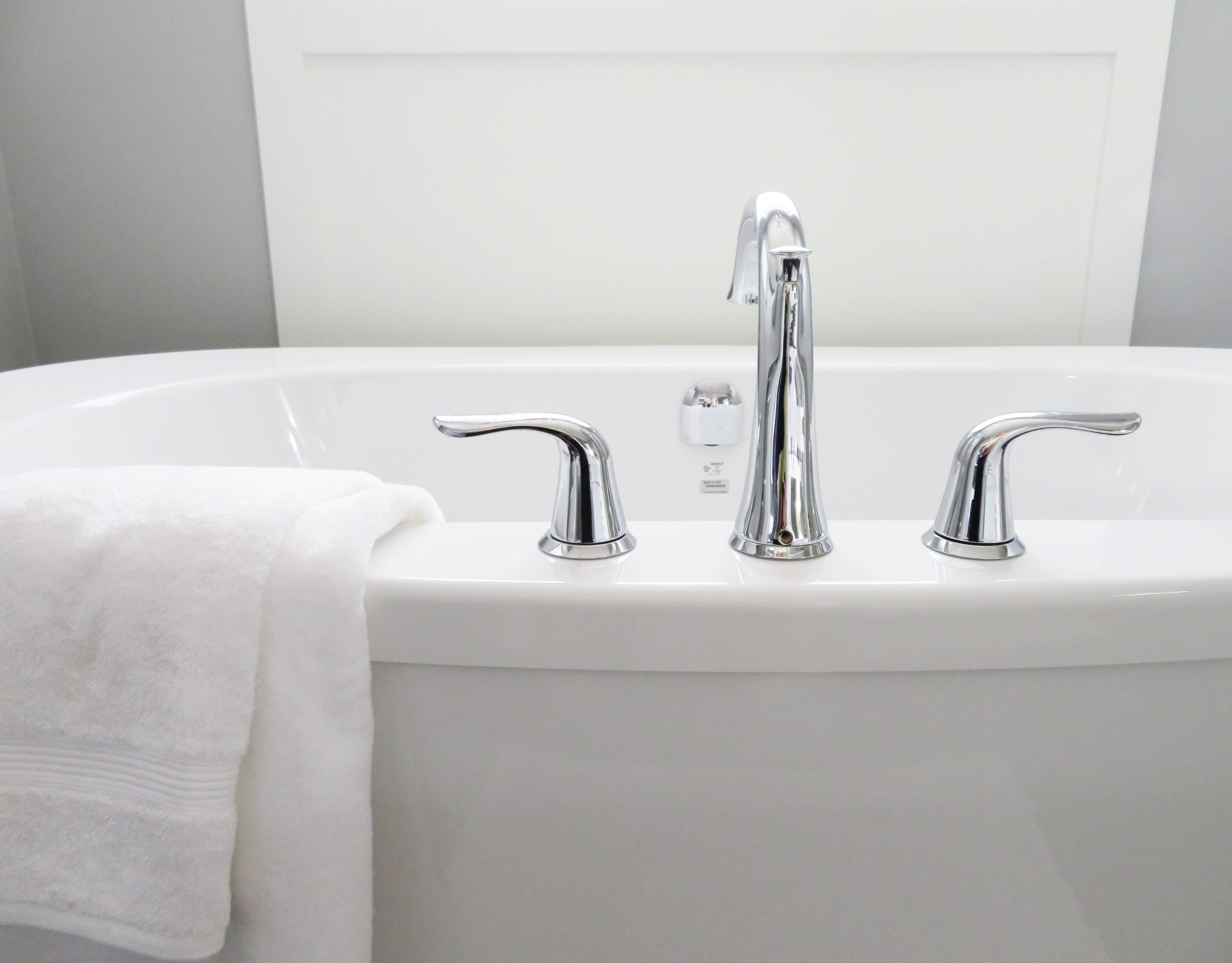 A polished faucet and handles on a bathtub. A white towel is draped over the side of the tub.
