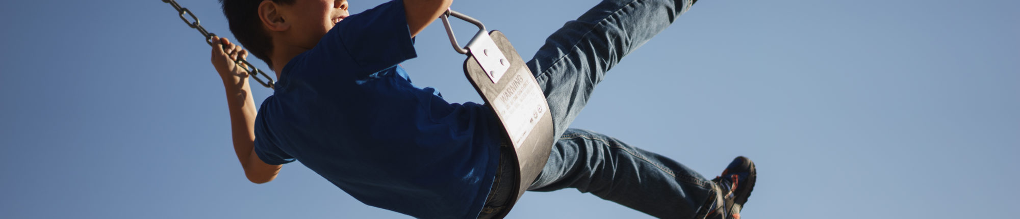 Young boy in blue shirt and jeans plays on a swing