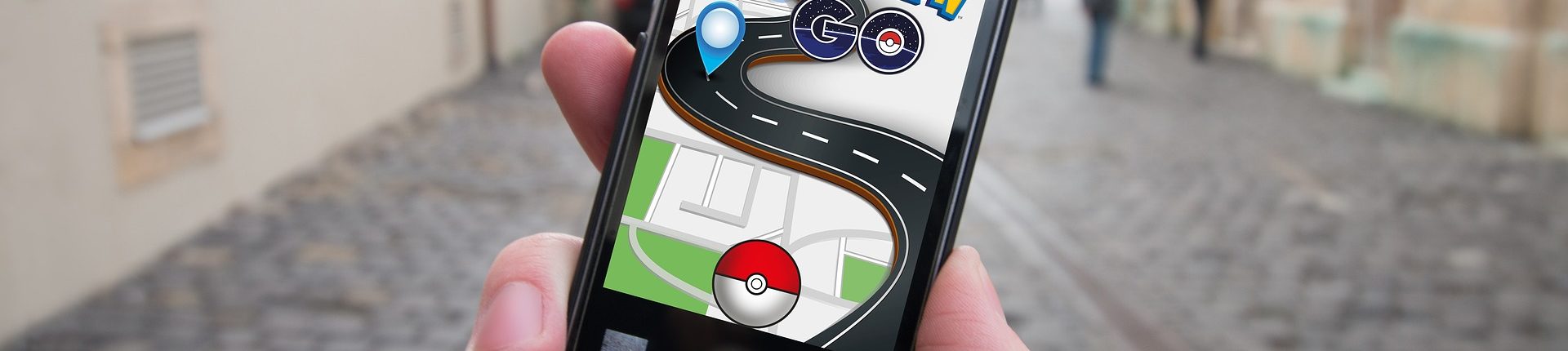 Close-up of a hand holding a phone open to the Pokémon GO app in front of a blurred street