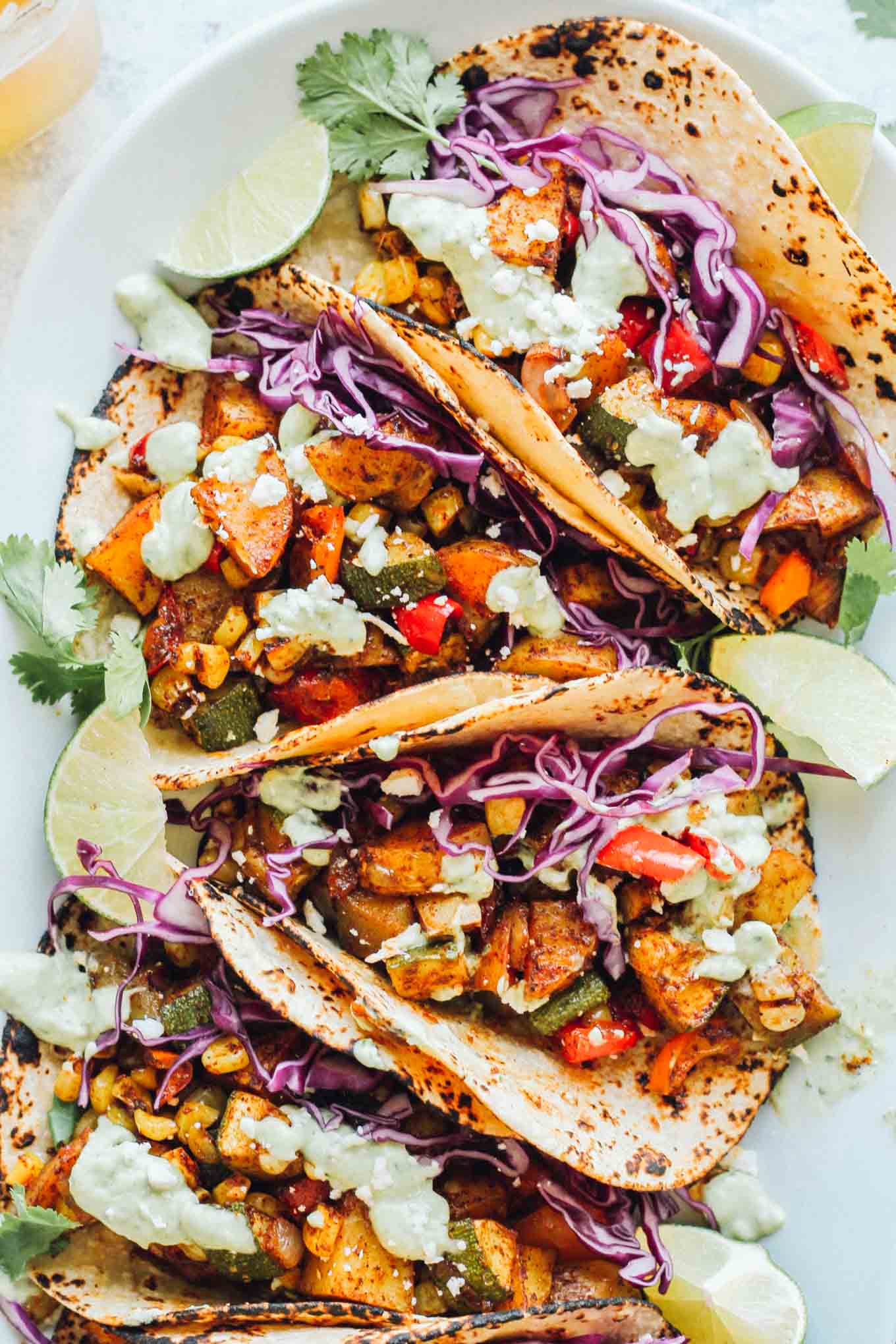 Top-down of several veggie tacos, filled with zucchini, corn, potatoes, onion, cabbage, and more