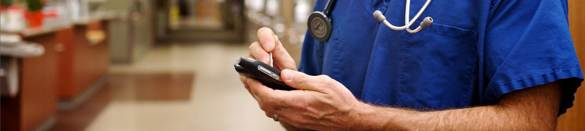 Male nurse is standing in hospital wing and using a mobile device for secure clinical messaging