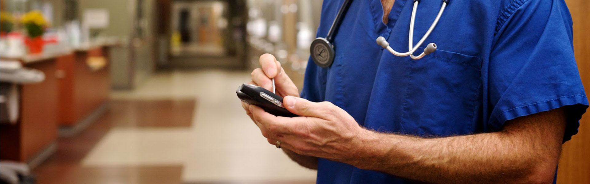 Male nurse is standing in hospital wing and using a mobile device for secure clinical messaging