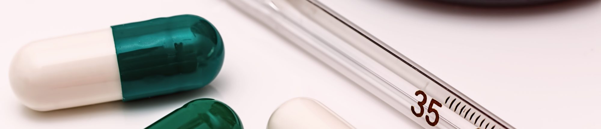 Extreme close-up of a half-white, half-teal pill, two other pills and a thermometer partially shown