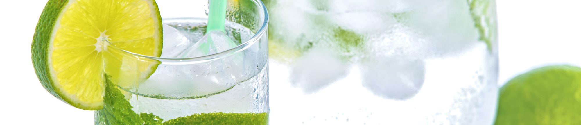 A close up of a glass of water with a lime garnish in front of a pitcher of water