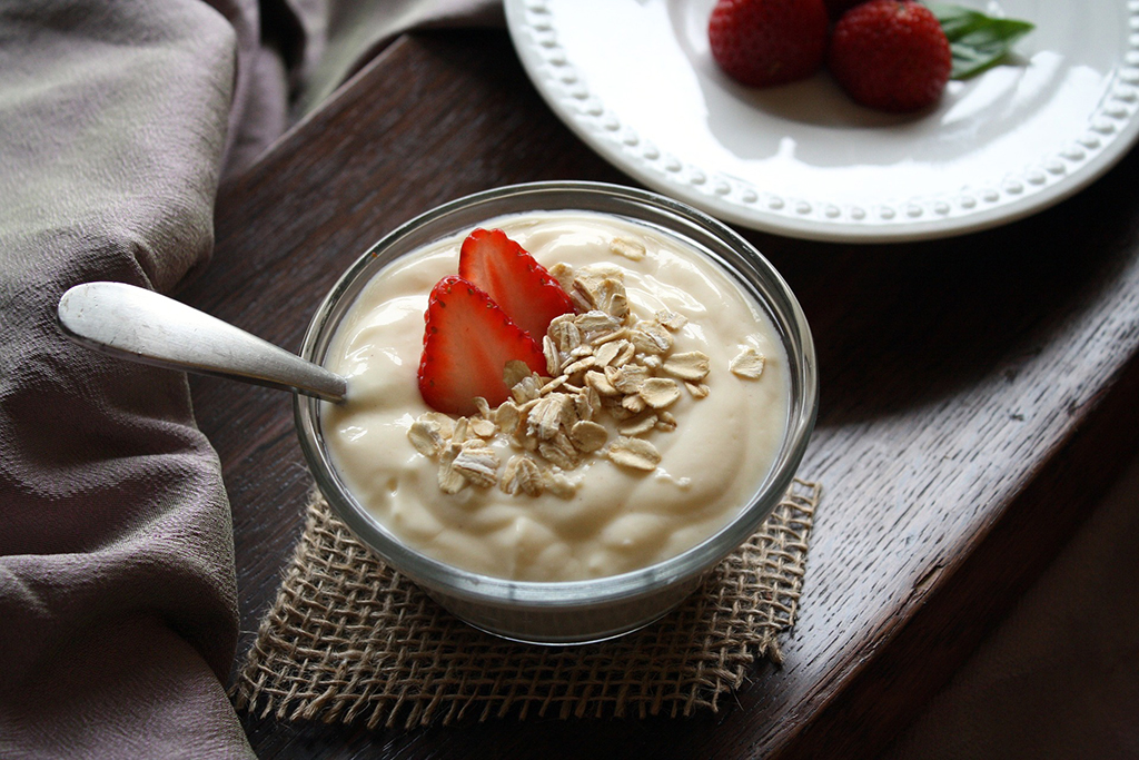 Close-up of yogurt with almond slivers and strawberry pieces. Food is in color, table is grayscale