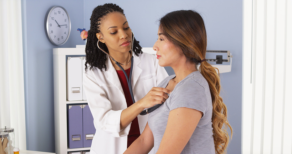 Doctor pressing stethoscope against female patient chest to check heart sounds in medical exam room