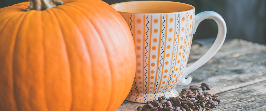 A pumpkin sits next to a coffee mug with a small pile of beans in the foreground
