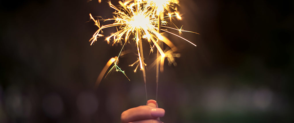 A close up on a woman's hand holding two sparklers, both are lit