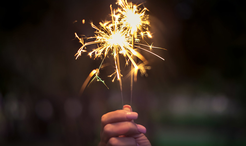 A close up on a woman's hand holding two sparklers, both are lit