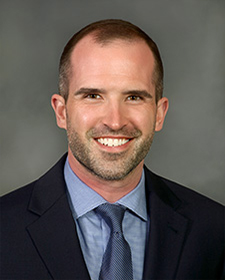 Portait of Carl Sizer wearing a suit, light blue shirt, and dark grey tie