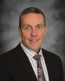 Portrait of George Garrow wearing a dark suit, striped shirt, and floral tie