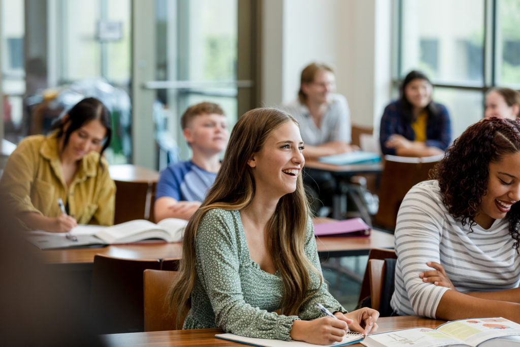 The college students take notes during lecture for reference later.