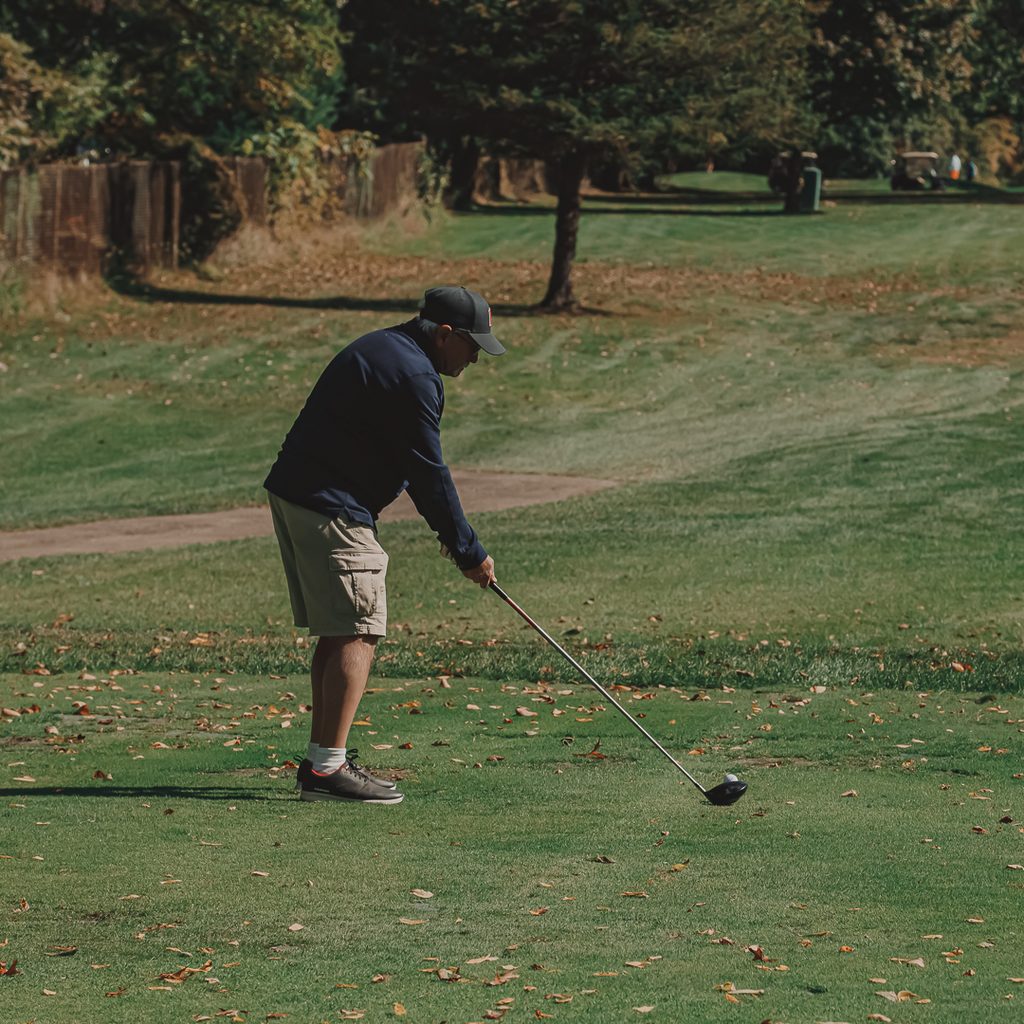 A male golfer in a black pull over golfing