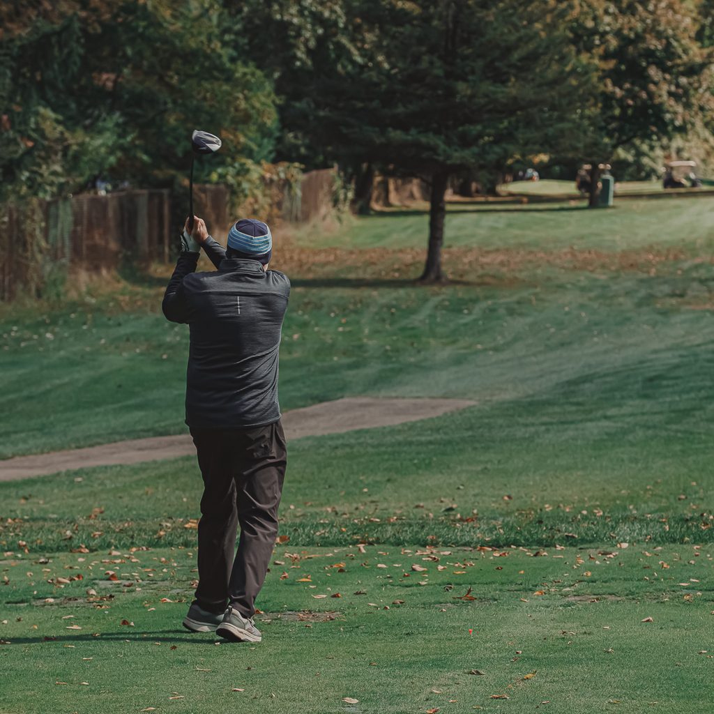 A male golfer in a blue hat driving