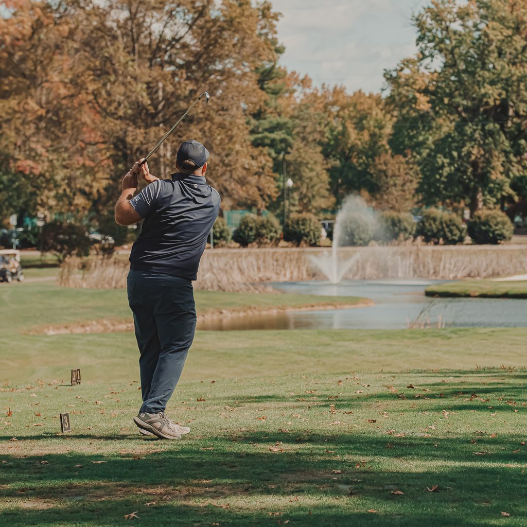 A male golfer driving with a fountain in the background