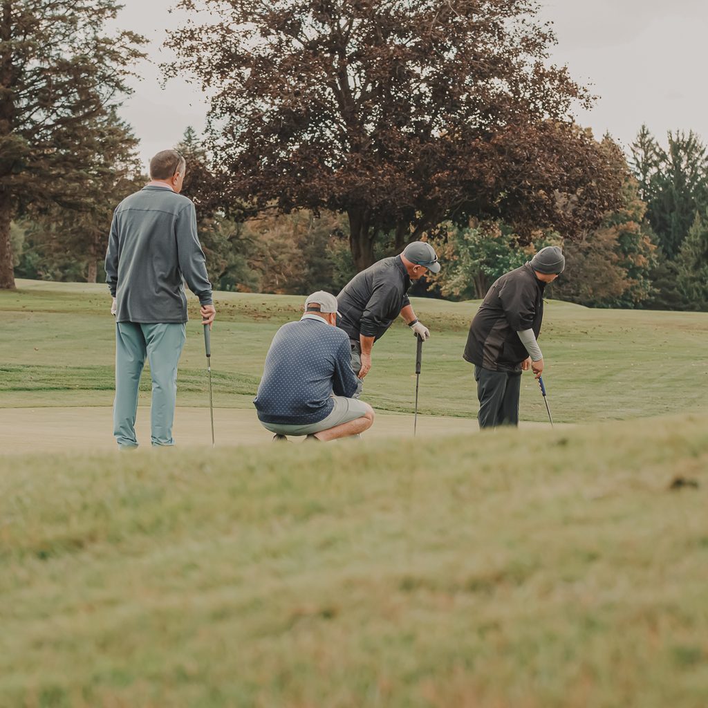 A group of male golfers watching their teammate putt