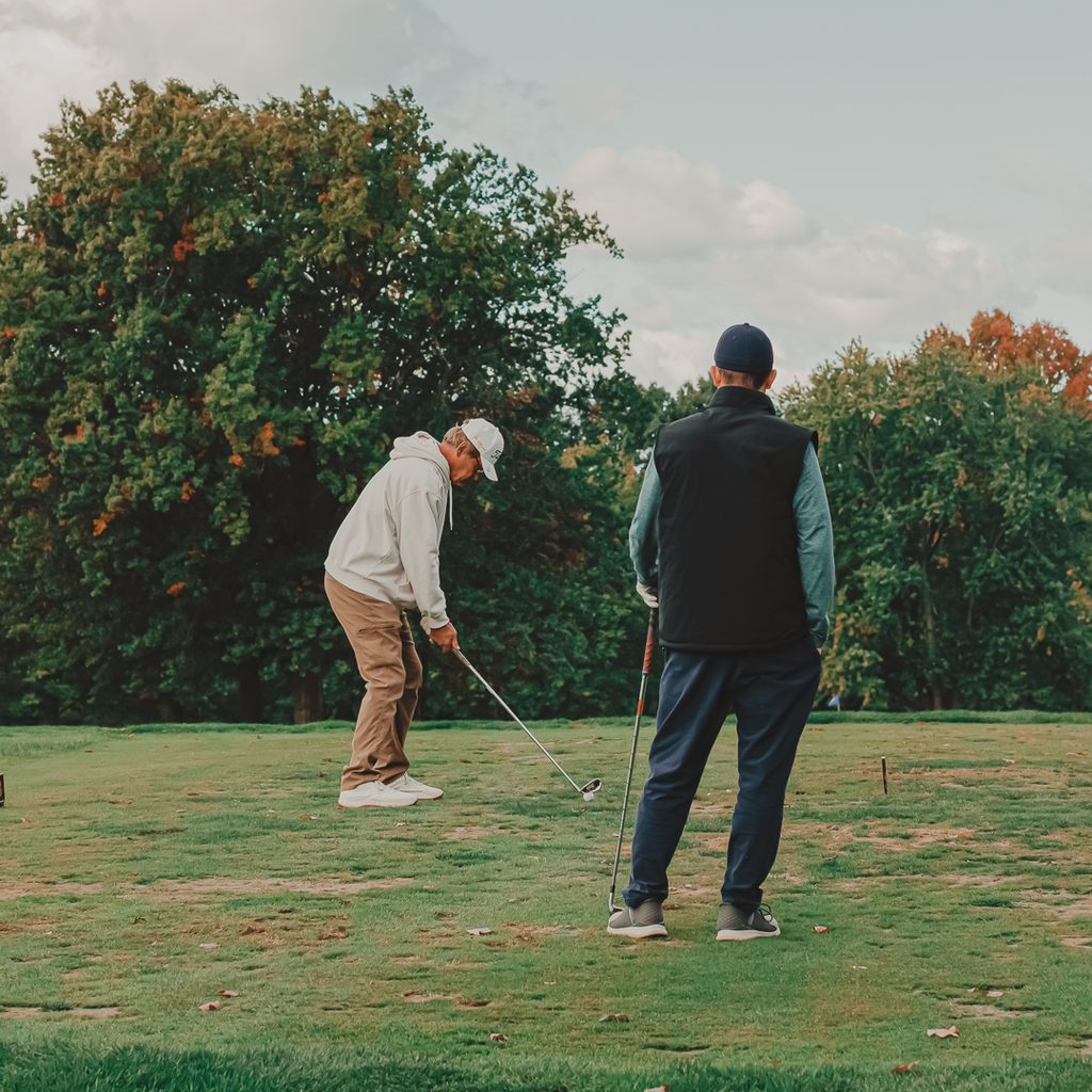 A male golfer watching his teammate chip in