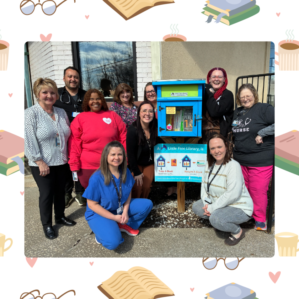 Group of healthcare workers posing around a blue Little Free Library box outside a building on a sunny day.