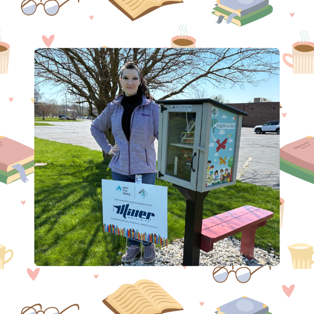 Person standing next to a Little Free Library box on a sunny day with a sign showing Miller Industries as a sponsor.